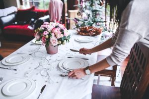A photo of a woman setting a table with silverware and two plates.