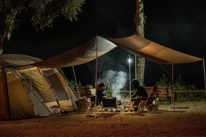 Two people near a fire by a tent outside,